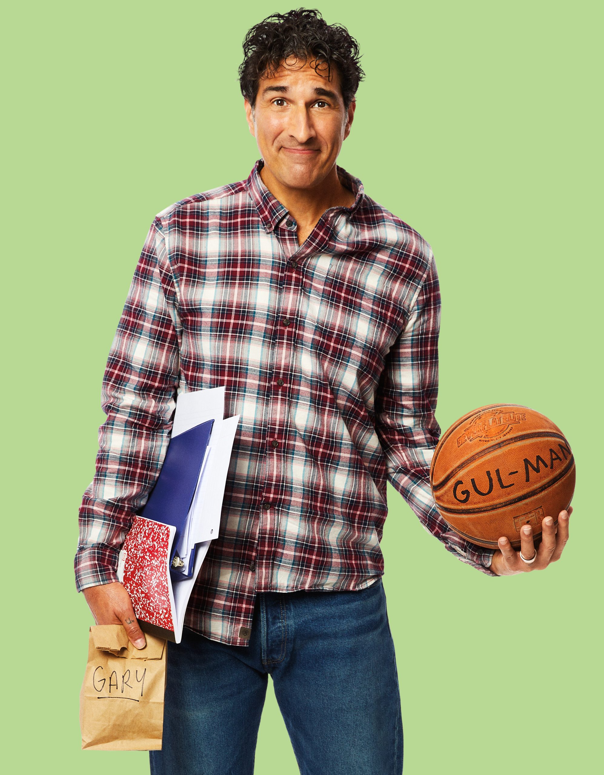 professional headshot of gary gulman that has a brown background. The man is wearing a brown shirt has shoulder length brown hair and is staring at the camera with his hand on his chin.